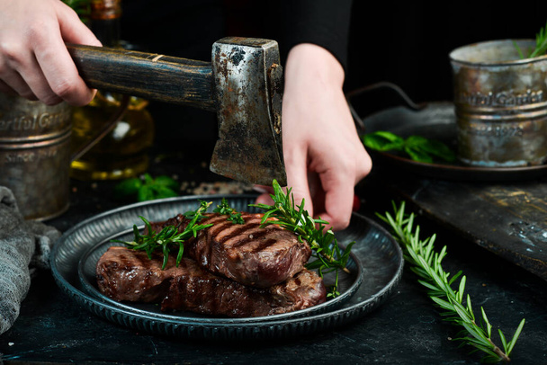 Two grilled ribeye beef steak on a plate in the hands of the chef. Food banner. On a black background. - Фото, изображение