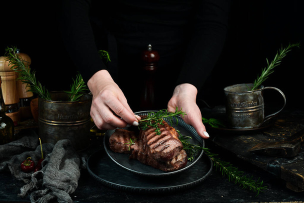 Two grilled ribeye beef steak on a plate in the hands of the chef. Food banner. On a black background. - Fotó, kép