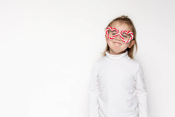 Funny surprised little girl child in caramel glasses and closed eyes in white background. Copy space for text - Foto, immagini