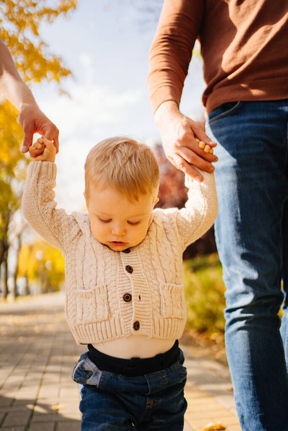 a cute little blonde boy in a beige jacket walks hand in hand with parents - Fotografie, Obrázek