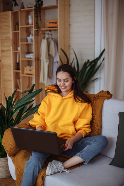 Young girl working at home on the couch with a laptop - Foto, afbeelding