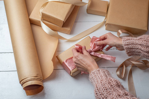 Gift wrapping in kraft paper. Gift wrapping in kraft paper. Females hands wrap boxes with gifts and tie bows made of bright ribbon - Valokuva, kuva