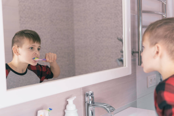 Μικρό ξανθό αγόρι Μαθαίνοντας να βουρτσίζετε τα δόντια του στο εσωτερικό λουτρό. Το παιδί μαθαίνει πώς να μείνετε υγιείς. Έννοια της υγειονομικής περίθαλψης. - Φωτογραφία, εικόνα