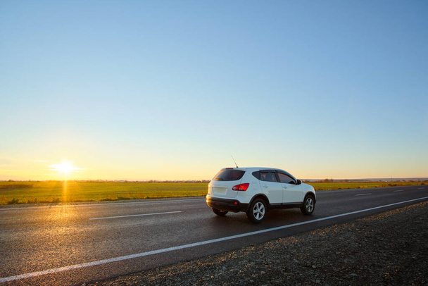 Samochód SUV jadący szybko po drodze międzymiastowej o zachodzie słońca. Wieczorem ruch na autostradzie - Zdjęcie, obraz