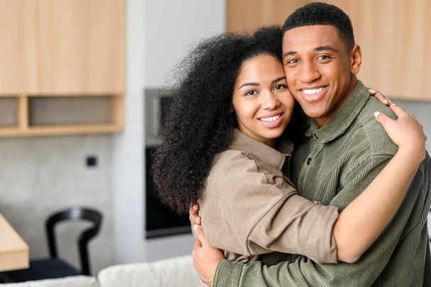 Close-up of happy multiracial couple posing while standing at the kitchen with blurred background. Happy owners of new flat smiling and embracing - Zdjęcie, obraz