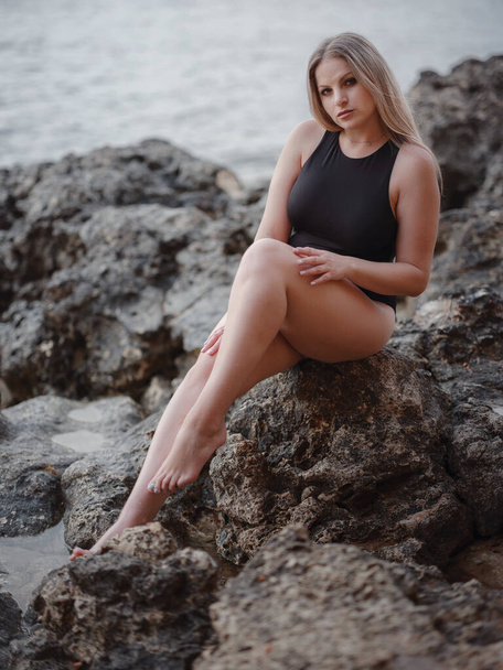 Porträt einer attraktiven blonden Amerikanerin mit langen Haaren, die am felsigen Strand posiert. Schöne Plus-Size - Foto, Bild