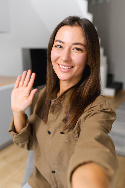 Happy asian woman holding smartphone and waving with hand to the camera while having video call with somebody - Foto, immagini