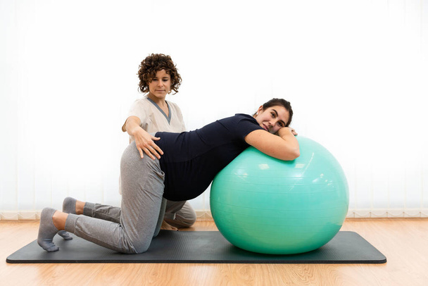 A pregnant woman doing pilates exercises with a ball with the help of her physiotherapist - Photo, Image