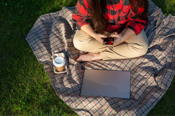 Workplace with laptop and cup of coffee on grass in garden. Working from home, freelance or remote work concept.   - Фото, изображение