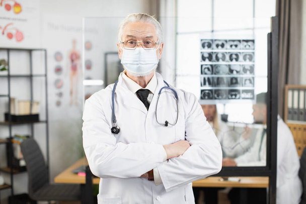 Senior physician in face mask posing with crossed arms - Фото, зображення