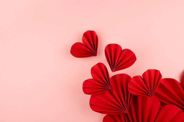 Bright red paper hearts of asian ribbed fans soar as flow on pastel pink background, top view, copy space. Festive wedding love backdrop for card, text, design, greeting, invitation, advertising. - Φωτογραφία, εικόνα