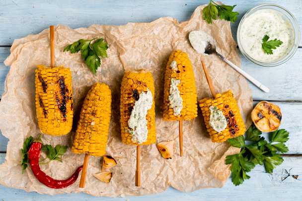 grilled corn on a blue wooden table with green sauce - Photo, Image