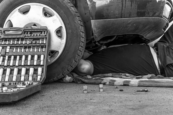 Automobile repair.Car repair.A person lies under the car repairing it and conducting an inspection and analysis of the breakdown. A set of keys at the wheel of a car in close-up. An auto mechanic - Fotografie, Obrázek