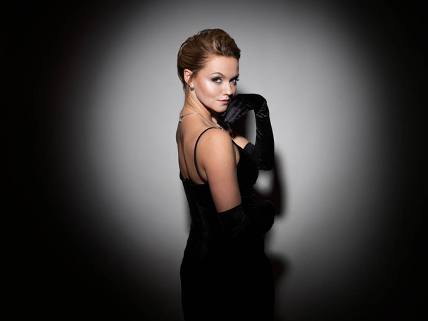 A femme fatale in a black dress with an open back and long velvet gloves. - Фото, изображение