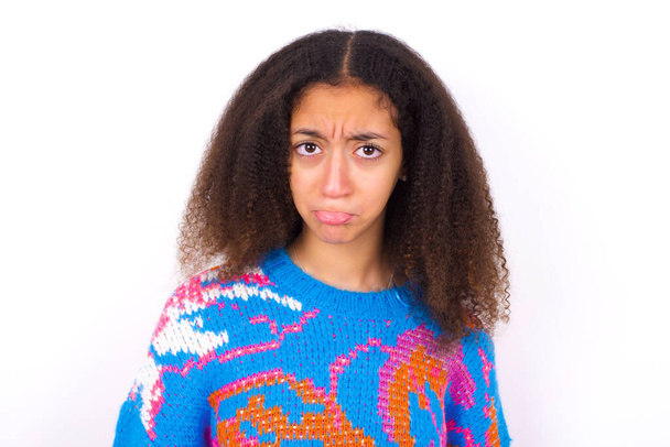African American teenager girl with afro hair style wearing vintage colourful sweater over white background depressed and worry for distress, crying angry and afraid. Sad expression. - Photo, Image