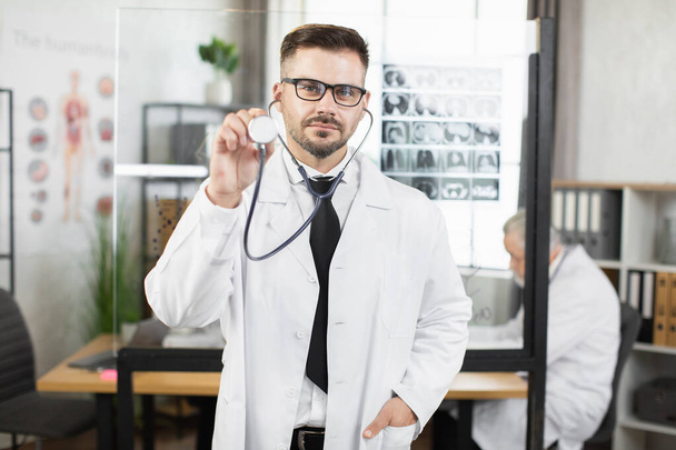 Doctor in lab coat and eyeglasses posing with stethoscope - Zdjęcie, obraz