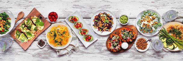 Healthy plant based low carb meal table scene. Overhead view on a white wood banner background. Cauliflower flatbread and steak, vegetable noodles, kale salads, avocados, sweet potatoes. - Fotografie, Obrázek