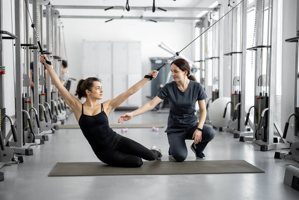 Женщина делает упражнения на декомпрессионных тренажерах с помощью специалиста по реабилитации - Фото, изображение