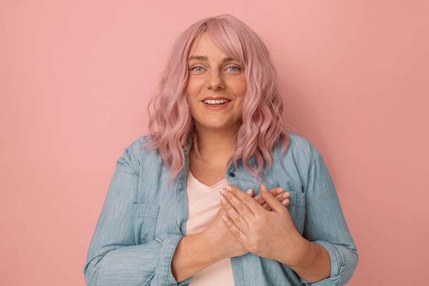 Mulher elegante atraente bonita segurar as mãos com as mãos no peito isolado em um fundo rosa, conceito de ajuda voluntário de saúde. - Foto, Imagem