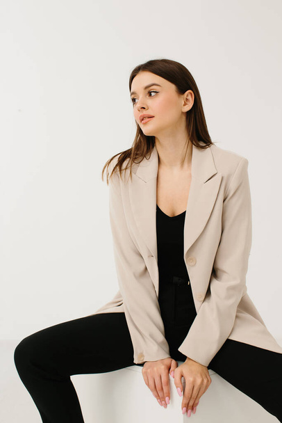 Young woman in trendy pastel suit sitting on cube against white background - Valokuva, kuva