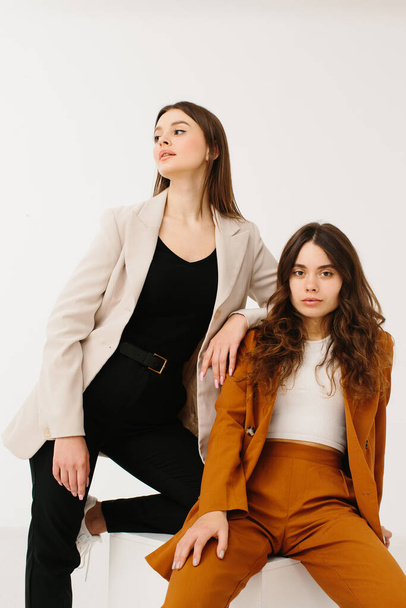 Model women dressed in fashionable pastel blazers and pants with stylish sneakers posing on a cube on a white background in the studio. - Photo, Image
