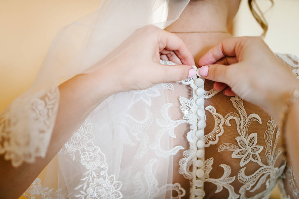 Bridesmaid helping bride fasten corset and getting her dress, preparing bride in morning for the wedding day. - Foto, Bild