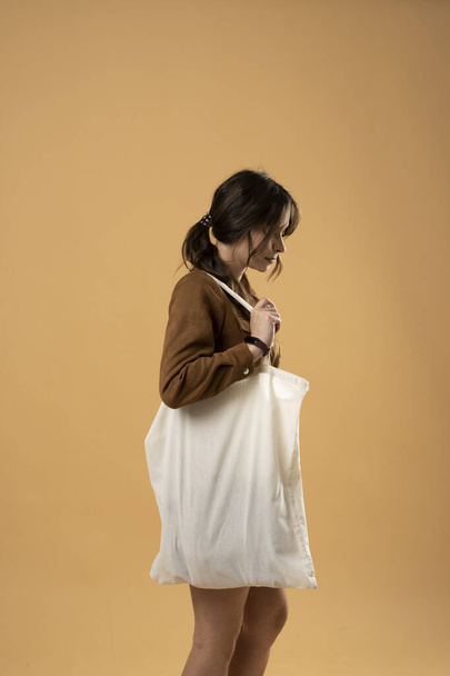 Woman with white cotton bag on a shoulder. Girl holding textile grocery bag with vegetables. Zero waste concept. - Photo, Image