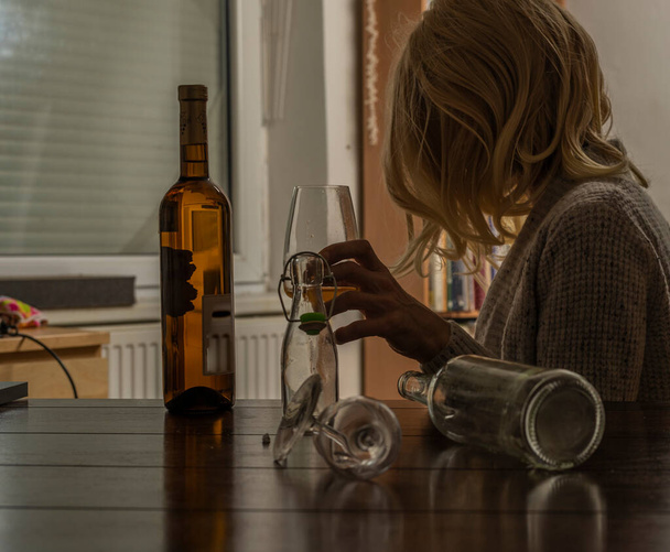 Femme aux cheveux blonds avec des bouteilles d'alcool à l'intérieur sombre - Photo, image