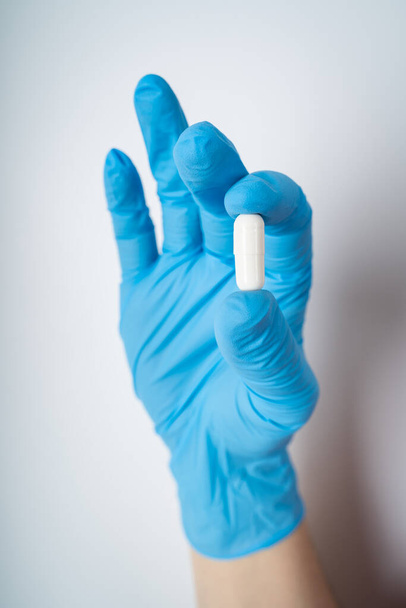 Female hand with blue medicine glove holding a pill - Foto, Bild