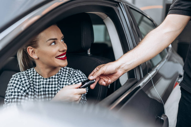 Satisfied and smiled female buyer sitting in her new car. She is smiling, looking at seller through open window while taking car keys from him.  - 写真・画像