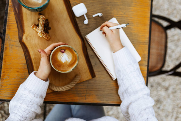 Руки девушки с чашкой кофе и пустым дневником с карандашом на деревянном столе - Фото, изображение