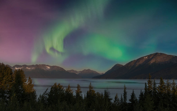 Kuzey Işıkları, Alaska 'daki Chugach dağlarında gün batımında güzel bir gölün üzerinde parlıyor. - Fotoğraf, Görsel