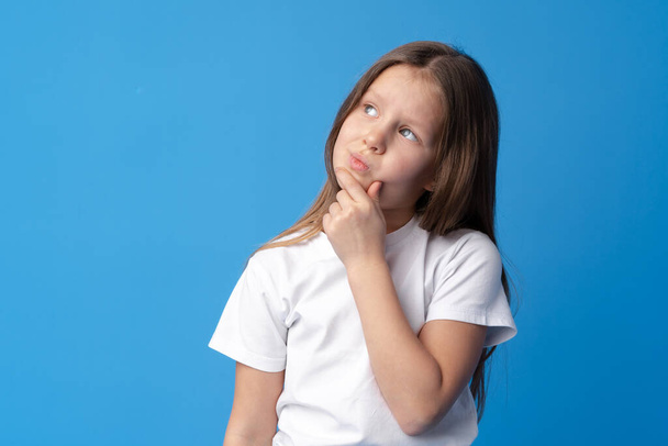 Little girl thinking and looking up over blue background - Fotografie, Obrázek