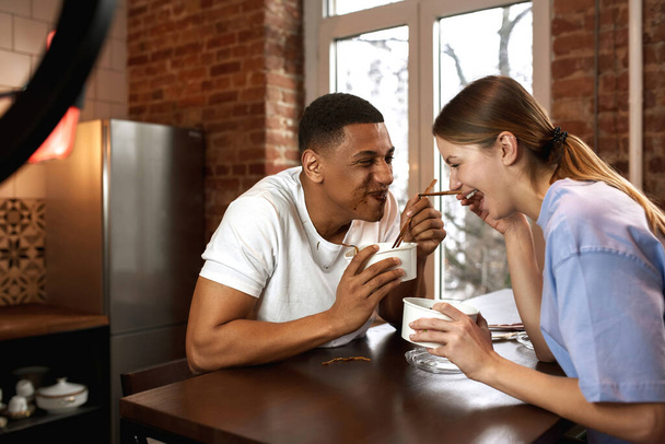 Cheerful multiethnic couple eat noodles for video - Foto, Bild