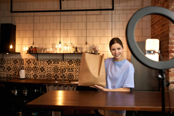 Girl showing paper bag with products for video - Valokuva, kuva