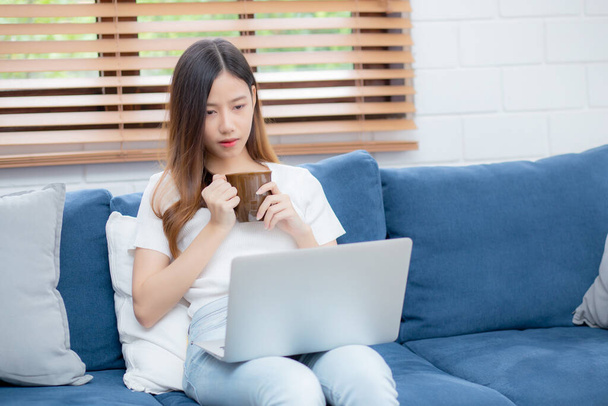 Young asian business woman smile and work from home with laptop computer online on sofa in living room, freelance girl using notebook and drink coffee on couch, new normal, lifestyle concept. - Foto, Imagen