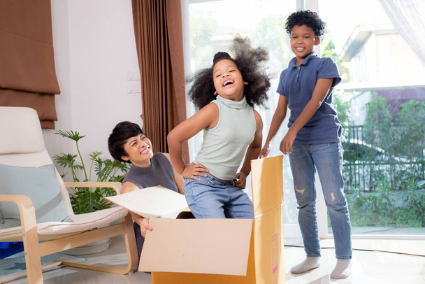 Felicidad Familia africana con madre e hijo e hija bailando dentro de la caja de cartón excitados juntos en la sala de estar en casa, mamá juguetona con los niños, relajación y ocio, conceptos familiares. - Foto, imagen