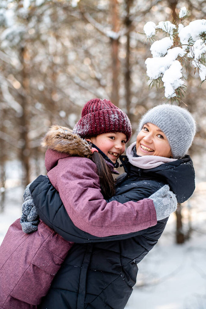 Családi téli séta az erdőben. Gyereknevelés, családi szokások. Anya és lánya jól érzik magukat télen az erdőben napsütéses, fagyos időben. Az anyák ölelése. - Fotó, kép