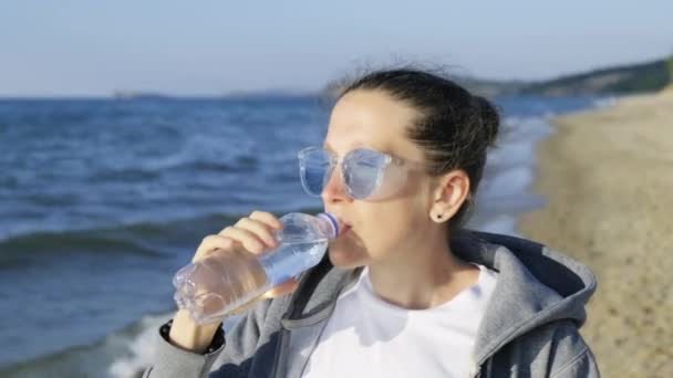 Ένα κορίτσι πίνει το πιο αγνό νερό της λίμνης Baikal, στέκεται στην όχθη της λίμνης Baikal με φόντο τη λίμνη Baikal. Αποθέματα γλυκού νερού - Πλάνα, βίντεο