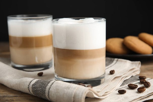 Delicious latte macchiato and coffee beans on wooden table - Φωτογραφία, εικόνα