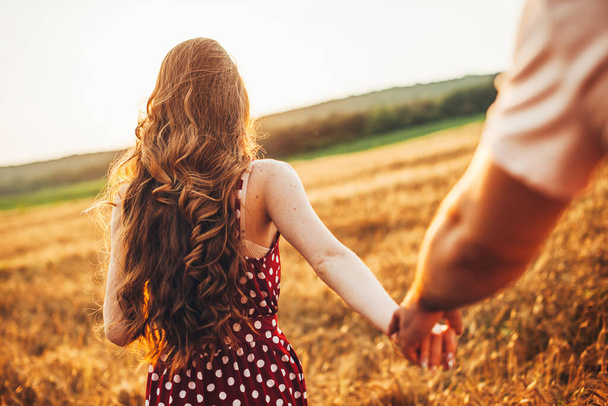 Rückansicht einer Frau mit langen roten Haaren, die ihre Freunde an der Hand hält und ihn durch das Weizenfeld zum Treffpunkt führt. Für die Konzeptgestaltung. Weizen - Foto, Bild