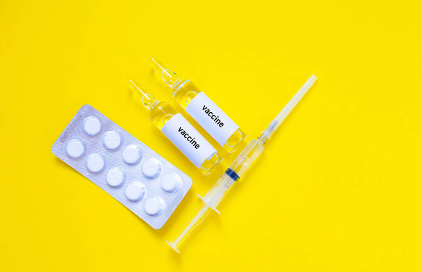 pilulky, injekční stříkačky a vakcinační ampulky na žlutém pozadí. Kvalitní fotografie - Fotografie, Obrázek