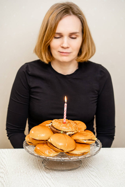a sad woman makes a wish and blows out a candle on a hamburger cake. - Foto, Imagem