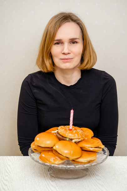 a woman makes a wish and blows out a candle on a hamburger cake. original cake.  - Foto, Imagem