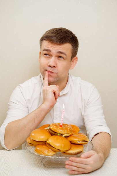 funny man makes wish and blows out candle on hamburger cake. cake for men. - Foto, Imagem