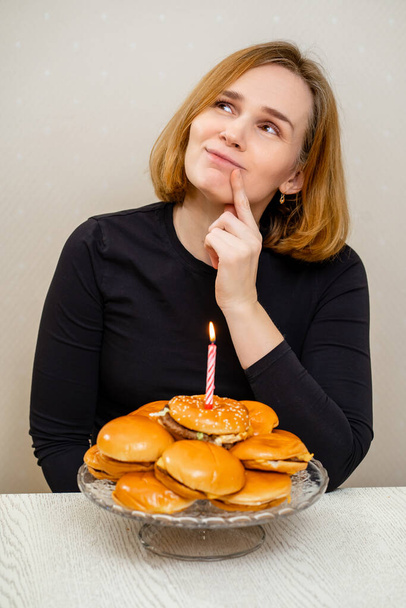 a funny woman makes a wish and blows out a candle on a hamburger cake.  - Foto, Imagem