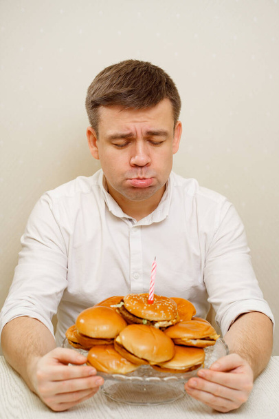 a sad man lights candles and makes a wish on a hamburger cake. cake for men. - Foto, Imagem