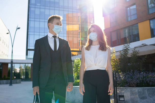 Позитивные молодые бизнесмены в медицинских масках разговаривают на улице - Фото, изображение