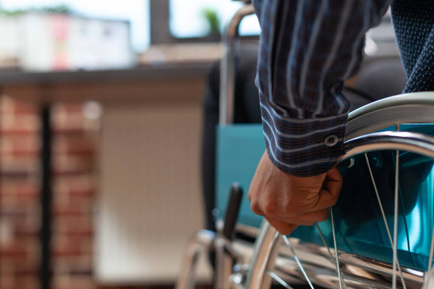 Primer plano de la mano del empleado de startup sosteniendo la llanta de la rueda de la silla de ruedas para moverse delante del escritorio - Foto, imagen