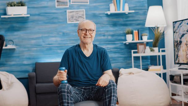 Портативный снимок пожилого человека, улыбающегося и держащего гантель - Фото, изображение